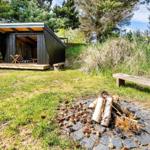 Holzhütte mit Sitzbank und Feuerstelle im Gras