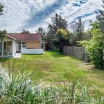 Haus mit Garten, Terrasse und Bäumen. Gras im Vordergrund.