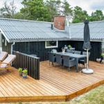 Haus mit großem Holzterrasse, Sitzgelegenheiten und Grillplatz.