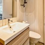 Badezimmer mit Waschbecken, Spiegel und Toilette. Holzfront und weiße Fliesen.