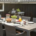 Außenbereich mit Tisch, Stühlen, Grill und Obstschale.