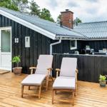 Schwarzes Holzhaus mit Terrasse, Liegestühlen und Grillplatz.