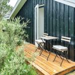 Hütte mit Holzterrasse, Tisch und zwei Stühlen. Umgeben von Grünflächen und Bäumen.