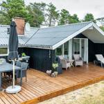 Terrasse mit Tisch, Stühlen und Liegen. Haus mit Holzverkleidung und Dach.