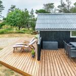 Holzterrasse mit Liegestühlen und Esstisch vor einem Haus mit grauem Dach.
