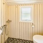 Badezimmer mit Toilette, Waschbecken und Dusche. Holzwände und Fliesenboden.