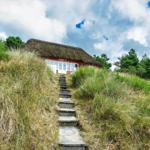 Haus mit Stiegenweg und Grasbewuchs unter blauem Himmel