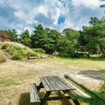 Holzpicknicktisch vor einem roten Haus mit Strohdach. Grünflächen und Bäume im Hintergrund.
