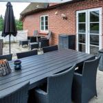 Terrasse mit Tisch, Stühlen und Sonnenschirm neben rotem Backsteinhaus.