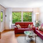 Wohnzimmer mit rotem Sofa, Glas-Tisch und Steinwand