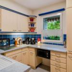 Küche mit hellen Schränken, blauer Fliesenwand und Fenster zum Garten.