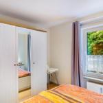 Schlafzimmer mit Doppelbett, Kleiderschrank und Fenster mit Blick auf Grün.