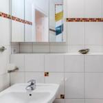 Badezimmer mit Waschbecken, Spiegelschrank und bunten Fliesenstreifen.