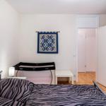 Schlafzimmer mit Bett, Wiege und Kleiderschrank. Wandbild und Holzboden sichtbar.