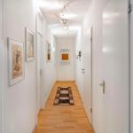 Flur mit Holzboden, Tapete und Bildern an den Wänden. Teppich und Tür sind sichtbar.