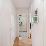 Flur mit Holzboden, weißen Wänden und Blick in Küche und Wohnbereich.