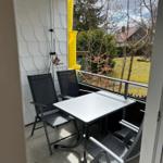 Balkon mit Tisch und Stühlen, rotem Sonnenschutz und Blick auf Grünflächen.
