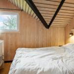Schlafzimmer mit Holzwand, Bett und Kinderbett. Fenster mit Blick auf Bäume.
