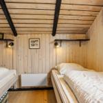 Zwei Betten in einem holzverkleideten Raum mit Deckenbalken und Wandregalen.