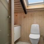 Badezimmer mit Toilette, Duschabtrennung und Dachfenster. Holzwände und weißer Fliesenboden.