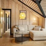 Wohnzimmer mit Sofa, Glas-Tisch und Holzwand. Decke mit Holzbalken.