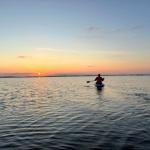 Ein Kajakfahrer paddelt auf ruhigem Wasser bei Sonnenuntergang.