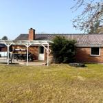 Ein Haus mit Terrasse, Grill und Garten. Ein Schornstein ragt aus dem Dach.