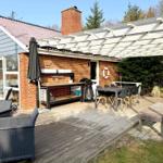 Terrasse mit Grill, Tisch, Stühlen und Sonnenschutz. Holzdecke und Gartenbereich.