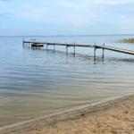 Holzsteg führt vom Strand ins Wasser. Boot liegt am Ende des Stegs.