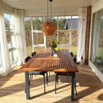 Terrasse mit Holztisch und Stühlen, großzügige Glaswände und Deckenleuchte.