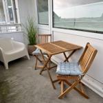 Terrasse mit Tisch, zwei Stühlen und Pflanze. Weiße Sitzgelegenheit daneben.