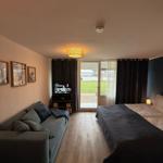 Bedroom with bed, sofa, and TV. Doorway to terrace with view of green area.