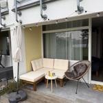 Terrace with seating group, round chair, and table under utility pipes.