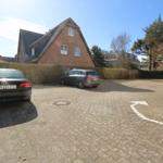 Zwei Autos parken auf einem gepflasterten Hof vor einem Haus mit Ziegelfassade.