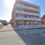 Viergeschossiges Wohnhaus mit Balkonen und weißen Geländern. Straßenansicht mit gepflastertem Weg.