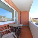 Terrasse mit Tisch und Stühlen, rote Ziegelwand und Blick auf Straße.
