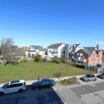 Grüner Rasenbereich mit geparkten Autos und Wohnhäusern im Hintergrund.