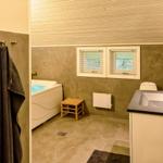 Badezimmer mit Badewanne, Waschbecken und Toilette. Zwei Fenster und Holzdecke.