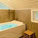 Bad mit Whirlpool, Dusche und zwei Fenstern mit Jalousien.