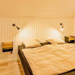 Schlafzimmer mit Doppelbett, zwei Nachttischen und Wandlampen an vertikal verkleideten Wänden.