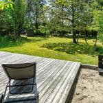Terrasse mit Grill, Liegestuhl und Sandkasten. Grasfläche und Bäume im Hintergrund.