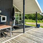 Terrasse mit Tisch, Stühlen und Sonnenschutz. Holzdecke und dunkler Holzwand. Grün hinter dem Haus.
