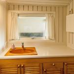 Badezimmer mit Waschbecken, Spiegel und Fenster mit Vorhängen.