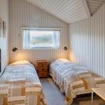 Zwei Betten mit gemusterten Bettdecken, Schreibtisch, Stuhl und Fenster mit Blick nach draußen.