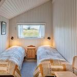 Zwei Betten mit gemusterten Decken, kleiner Nachttisch und Fenster mit Blick auf Gras.
