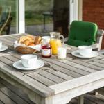 Holztisch mit grünen Sitzkissen und Frühstück auf der Terrasse.