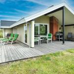 Haus mit Holzterrasse, Grill und grünen Stühlen im Freien.