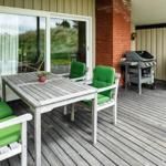 Terrasse mit grünen Sitzkissen, Tisch und Grill. Holzdecke und Glasfront.