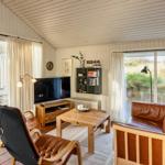 Wohnzimmer mit braunen Ledermöbeln, Holztisch und TV. Große Fenster mit Blick auf Grasland.
