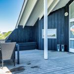 Terrasse mit Tisch, Stühlen und Sitzbank. Dunkelblauer Holzaufbau mit Glasfronten.